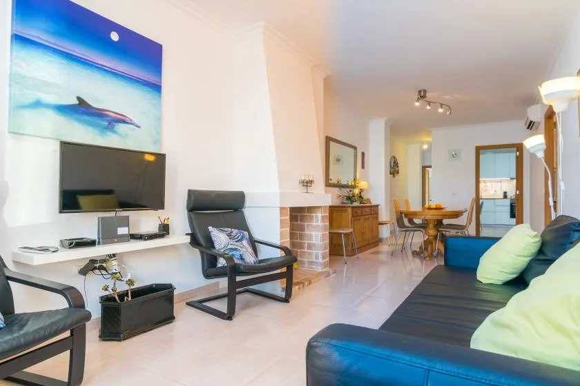 A living room with a television, seating, and a dining area in the background.