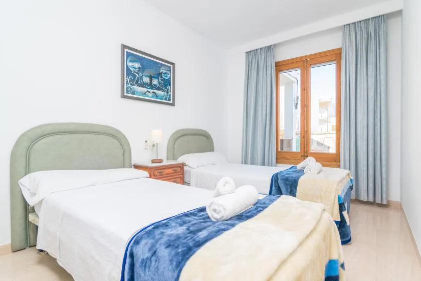 A bright bedroom with two beds, blue curtains, and a framed picture.