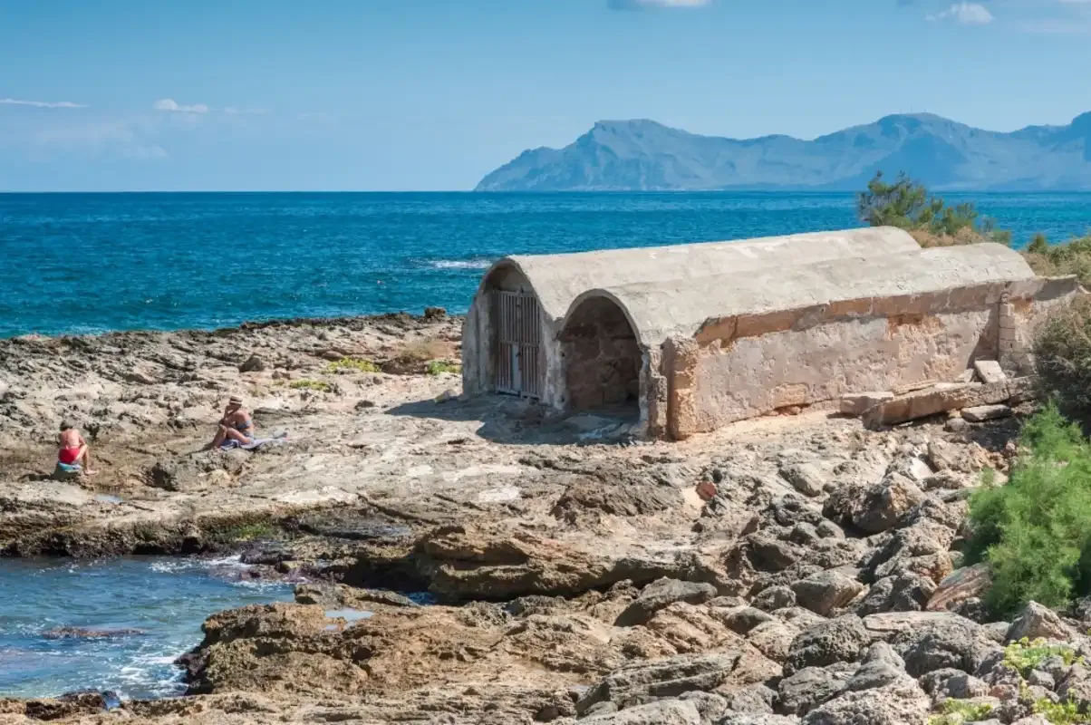 A stone structure stands on a rocky shoreline beside the sea.