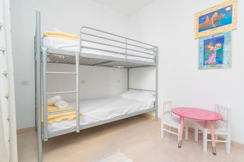 A bedroom with a metal bunk bed and a small pink table.
