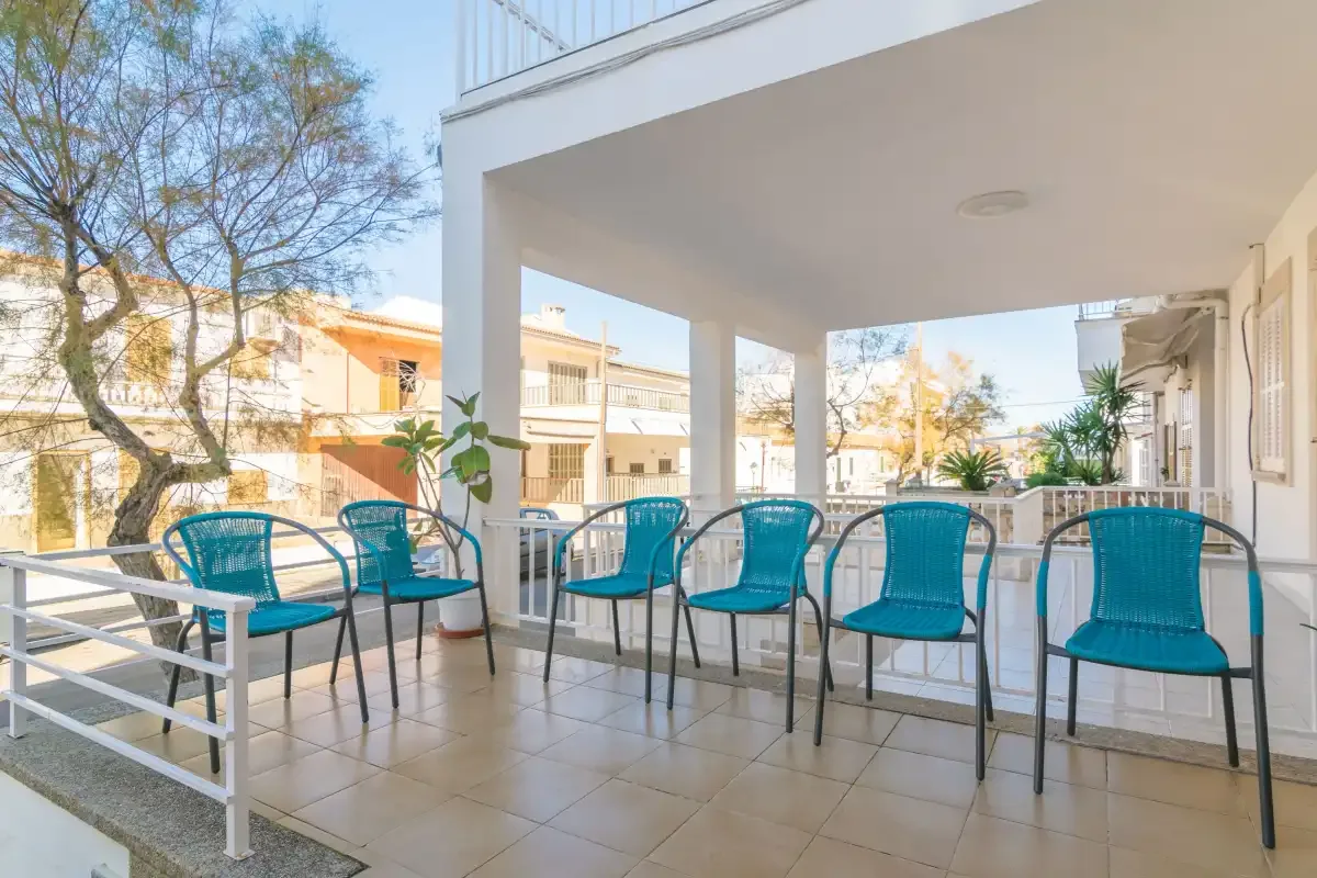 A covered outdoor seating area with turquoise chairs and a railing.