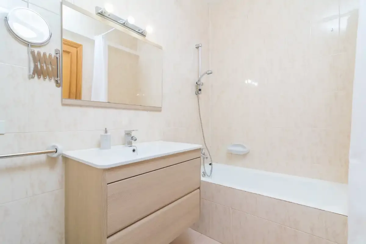 A bright bathroom with a vanity, mirror, and bathtub.