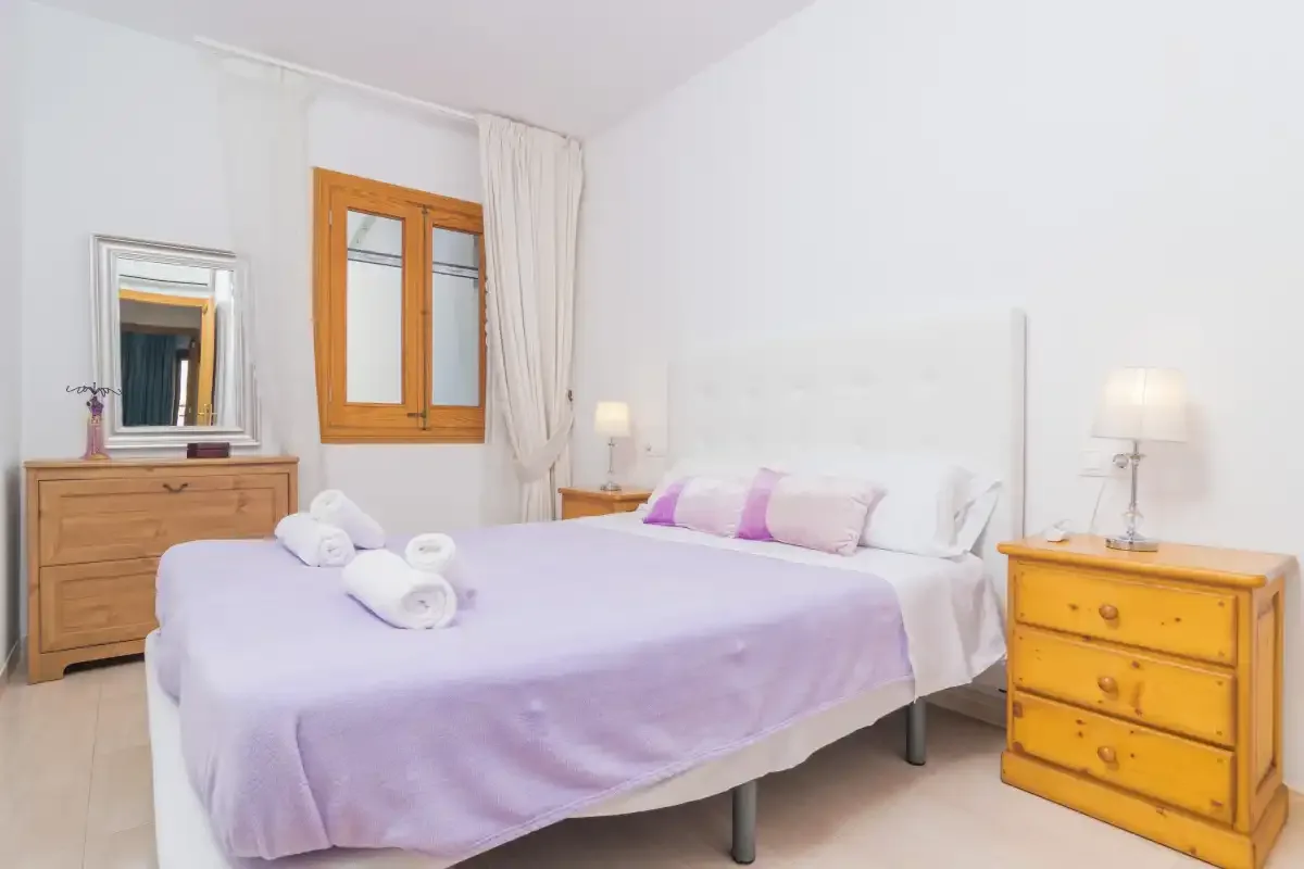 A bedroom with a double bed, bedside tables, and a window.