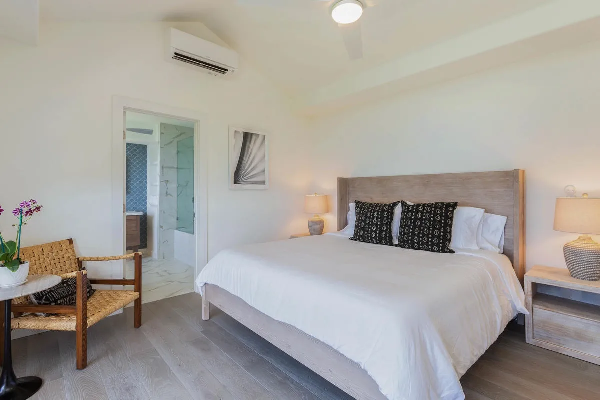 A bright bedroom with a large bed and a woven chair beside the doorway.
