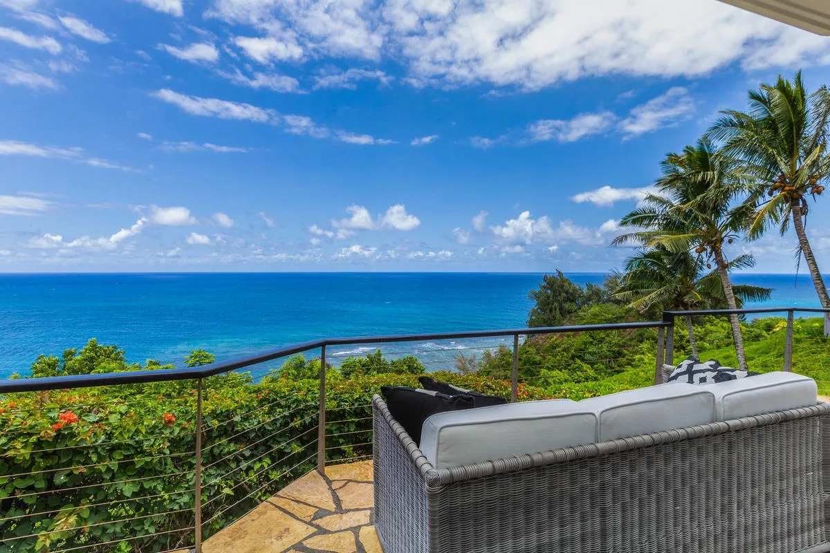 A tiled outdoor terrace overlooks the ocean, with seating beside the railing.