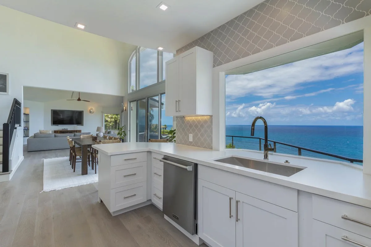 A bright kitchen with white cabinetry and a large window overlooking the ocean.