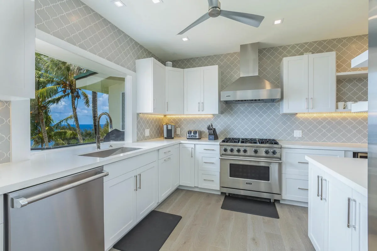 A bright kitchen with white cabinetry, stainless steel appliances, and a large window.