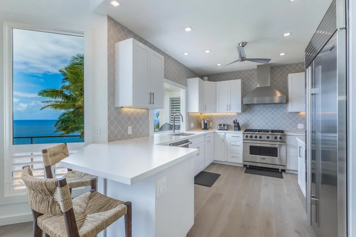 A bright kitchen with white cabinetry, a large island, and a view of the ocean.