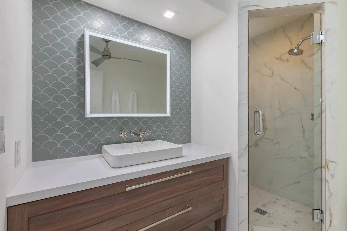 A bathroom with a vessel sink beneath a large mirror and a glass shower.