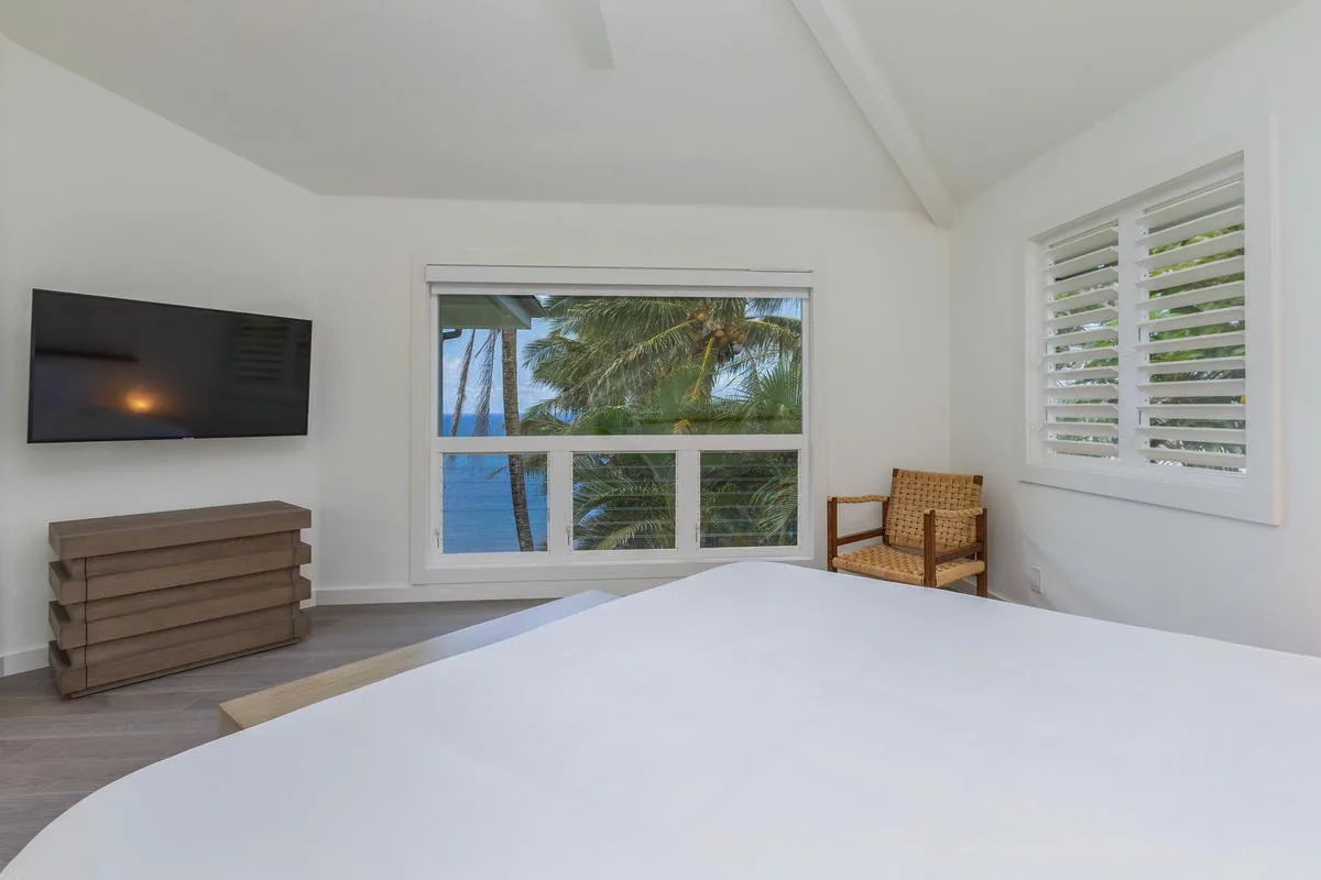 A bright bedroom with a large bed, a wall-mounted television, and tropical views.