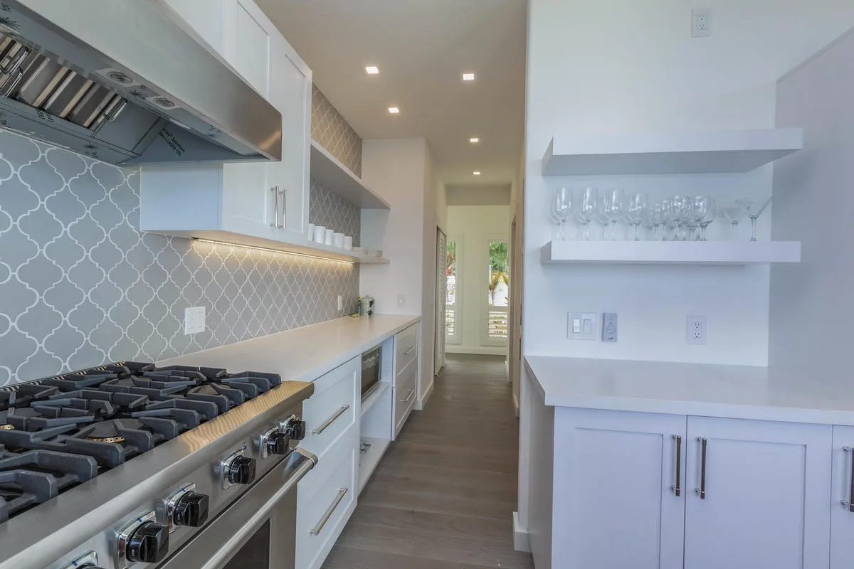 A modern kitchen with a long counter, gas cooktop, and open shelving.
