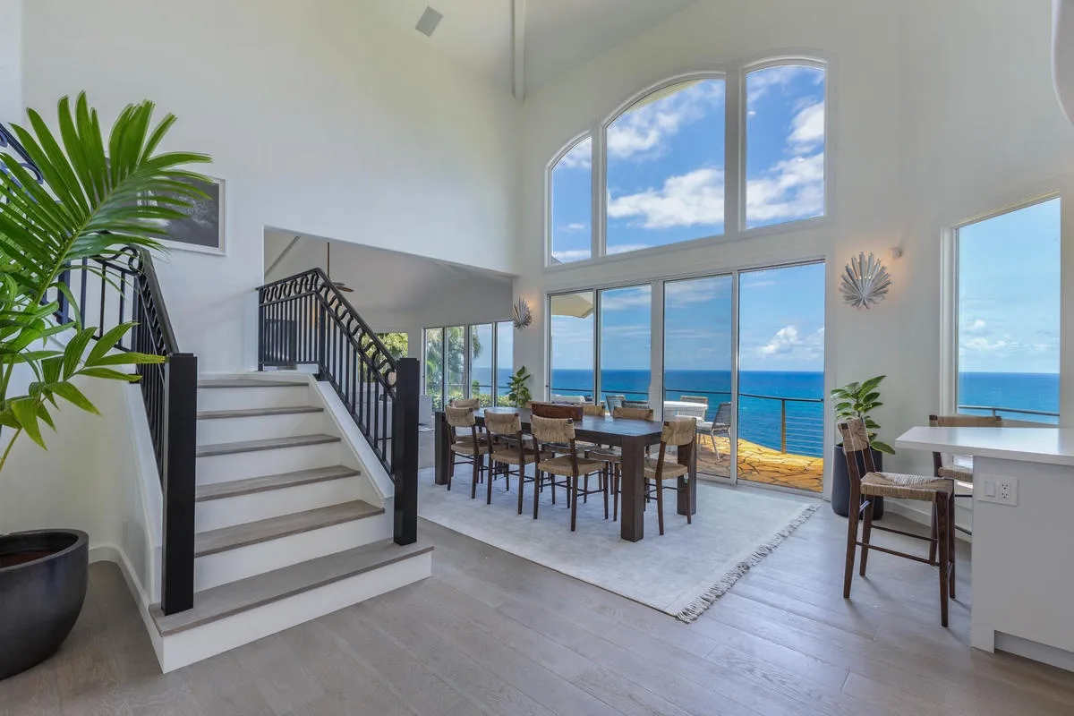 A bright dining area with a staircase and large windows overlooking the ocean.