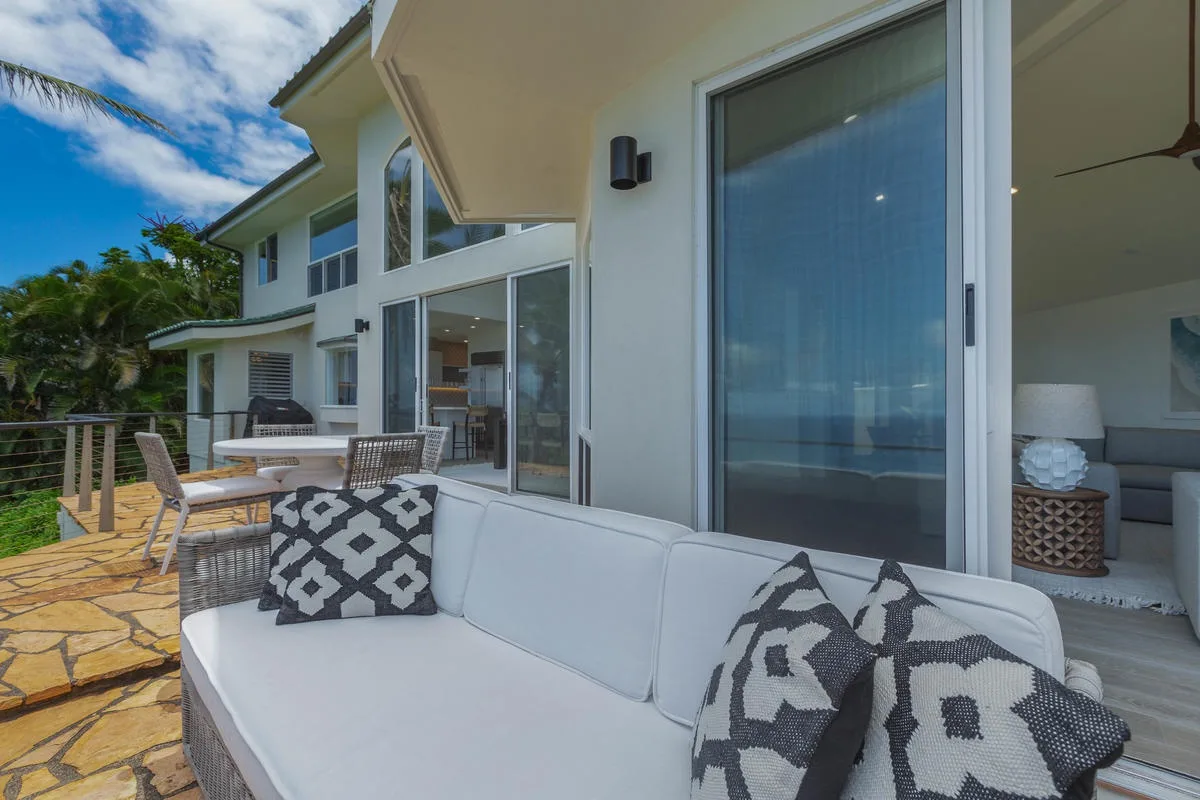 A white outdoor seating area overlooks the water beside large glass doors.