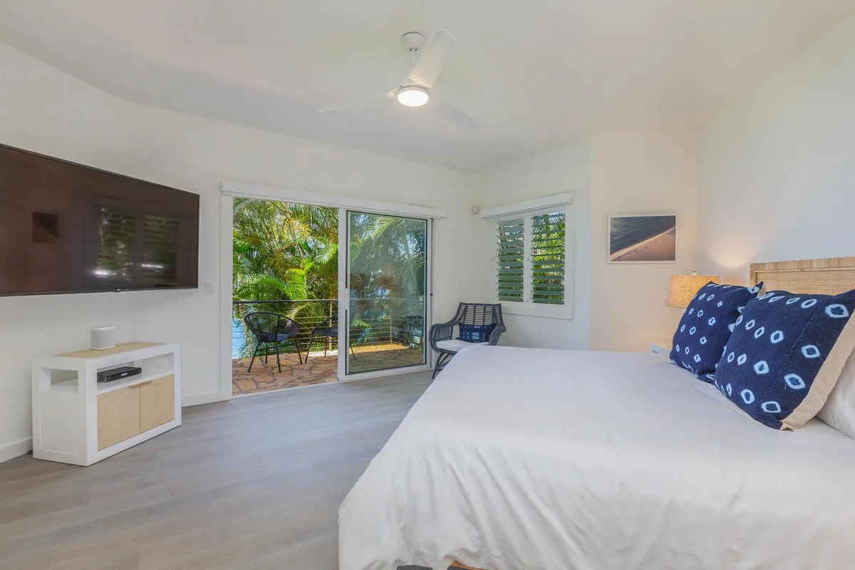 A bright bedroom with a large bed and sliding glass doors opening to greenery.