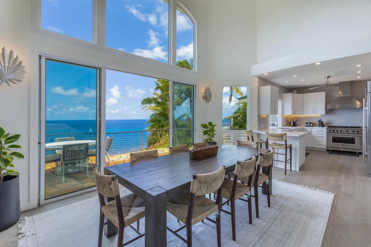 A bright dining area and open kitchen overlook the ocean through tall windows.