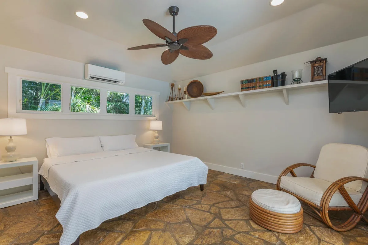 A bedroom with a neatly made bed, windows, and a ceiling fan.