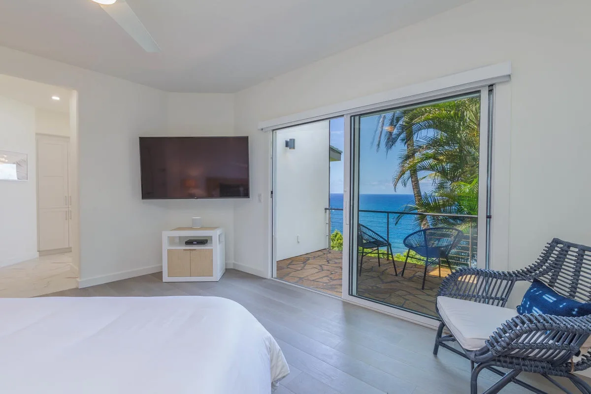 A bedroom opens onto a balcony with seating and a view of the ocean.