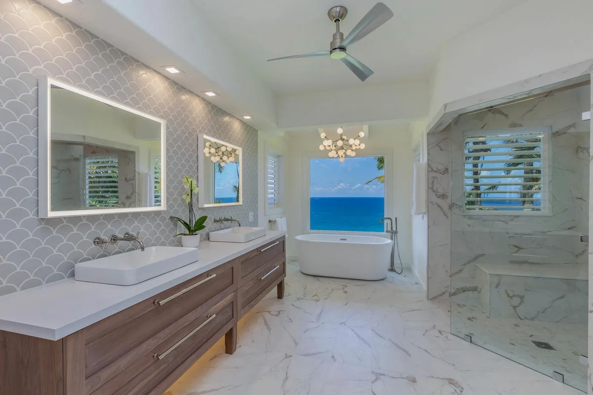 A bathroom with a double vanity, bathtub, and ocean view.