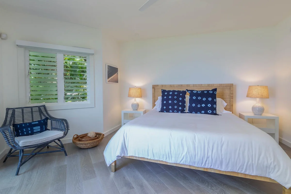 Bedroom with a white bed, matching bedside tables, and a window with shutters.