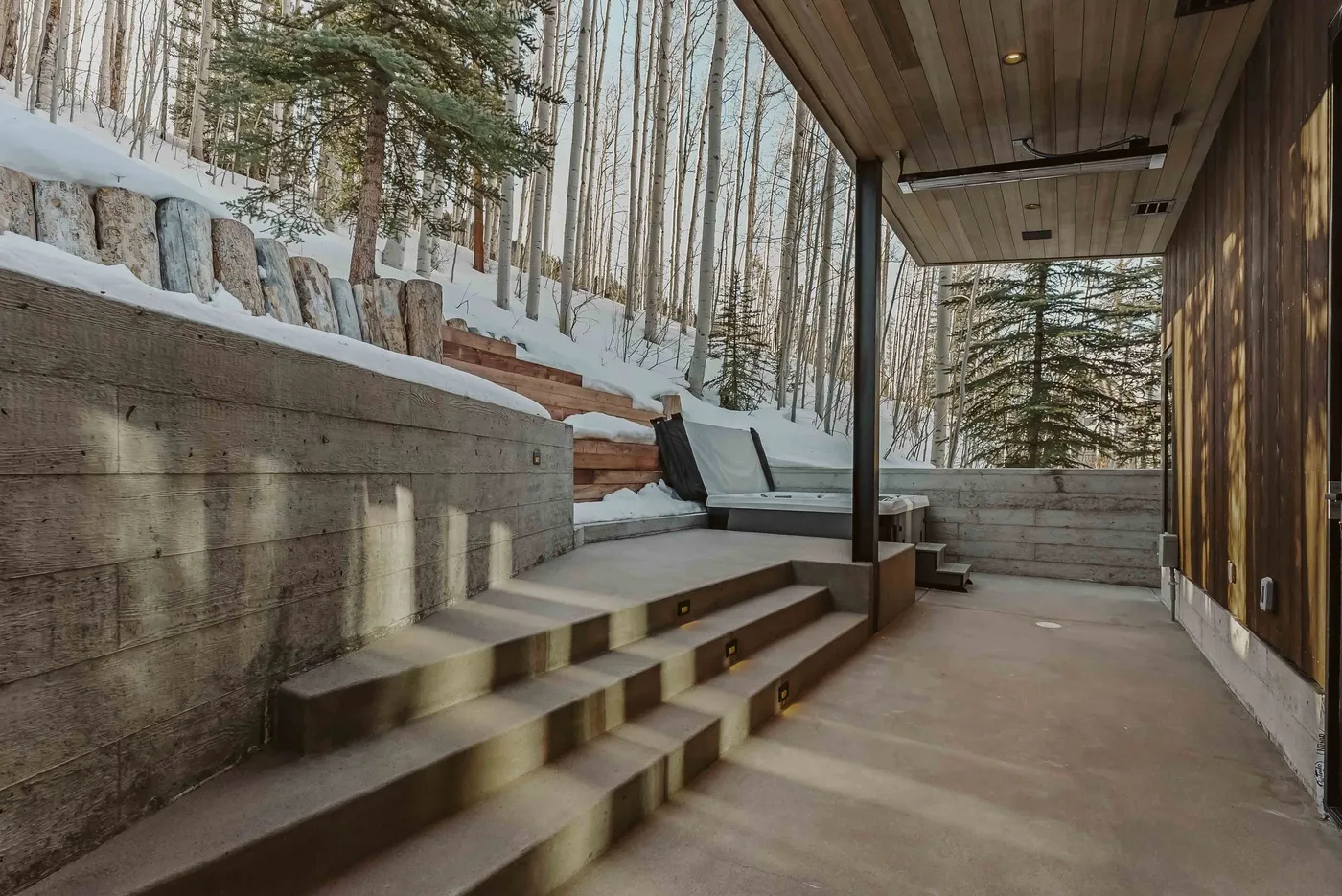 Patio exterior cubierto con escalones de hormigón y vistas a un bosque nevado.