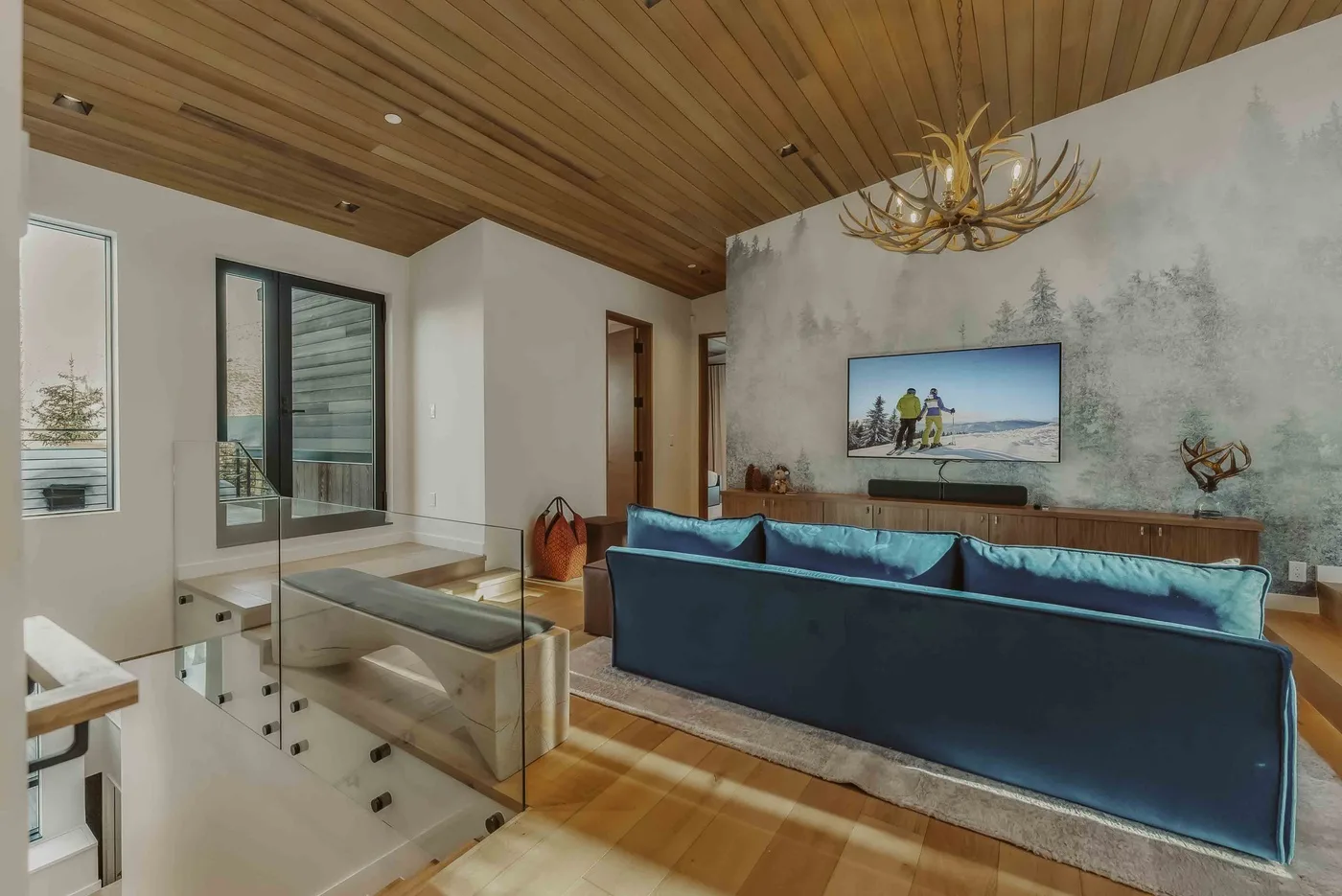 Una sala moderna con asientos azules, un televisor en la pared y un techo revestido de madera.