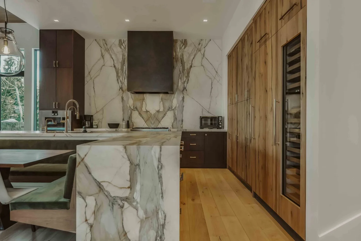 Una cocina moderna con isla de mármol, armarios oscuros y suelo de madera.