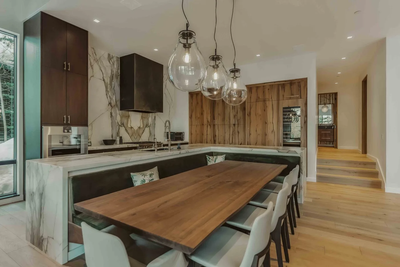 Una cocina moderna y comedor con una larga mesa de madera bajo lámparas colgantes.
