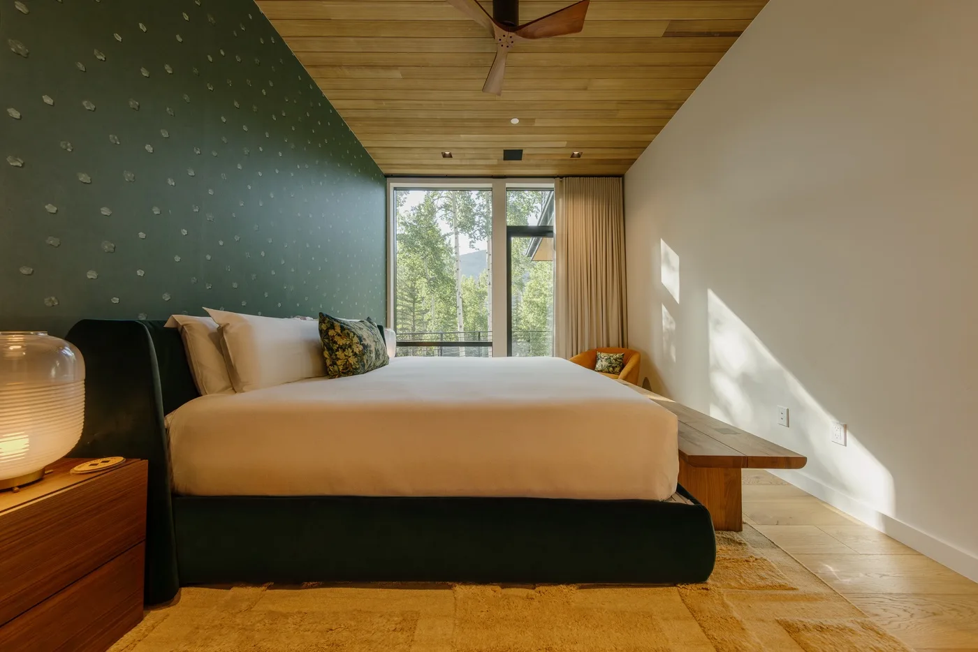 Un dormitorio con una cama frente a ventanas altas y una vista de vegetación.