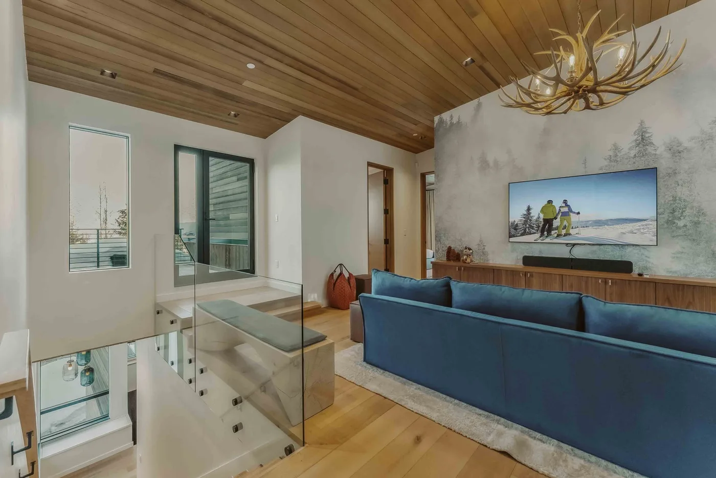 Una sala de estar moderna con asientos azules, un televisor y techo revestido de madera.