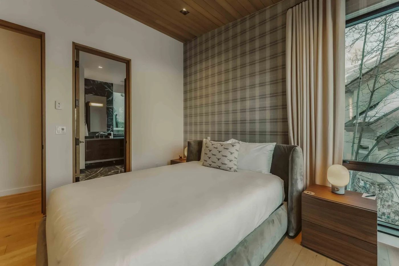 Un dormitorio con una cama bien tendida junto a una ventana grande.