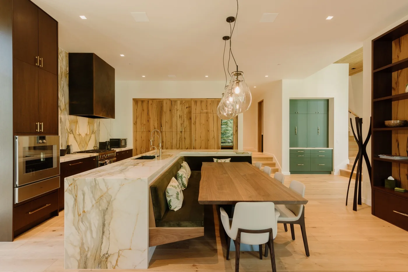 Cocina y comedor de planta abierta con una mesa larga de madera e isla de mármol.