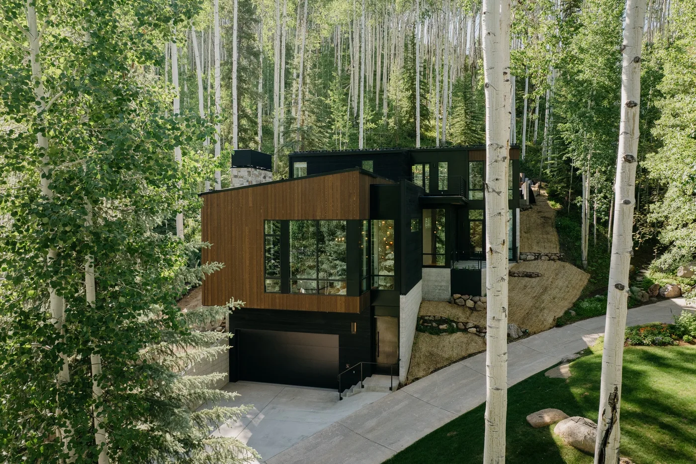 Una casa moderna se encuentra entre árboles altos, con una entrada pavimentada al frente.