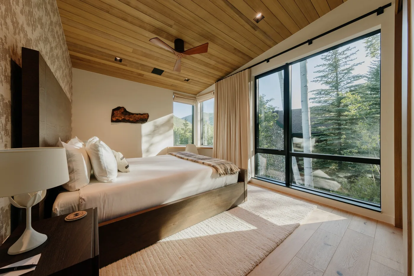 Un dormitorio con una cama junto a grandes ventanas con vistas a los árboles.
