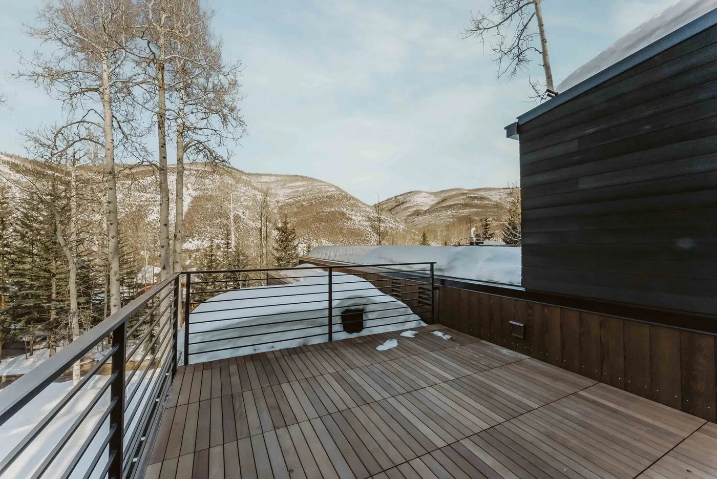 Una terraza de madera al aire libre da a un paisaje montañoso nevado.