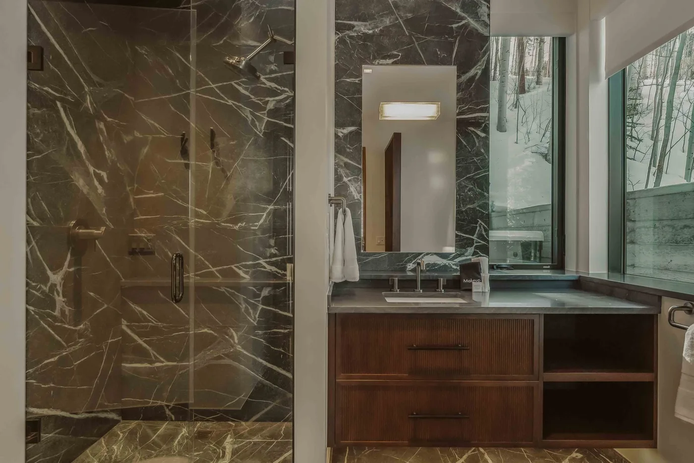 Un baño moderno con ducha de vidrio, mueble de madera y ventanas grandes.