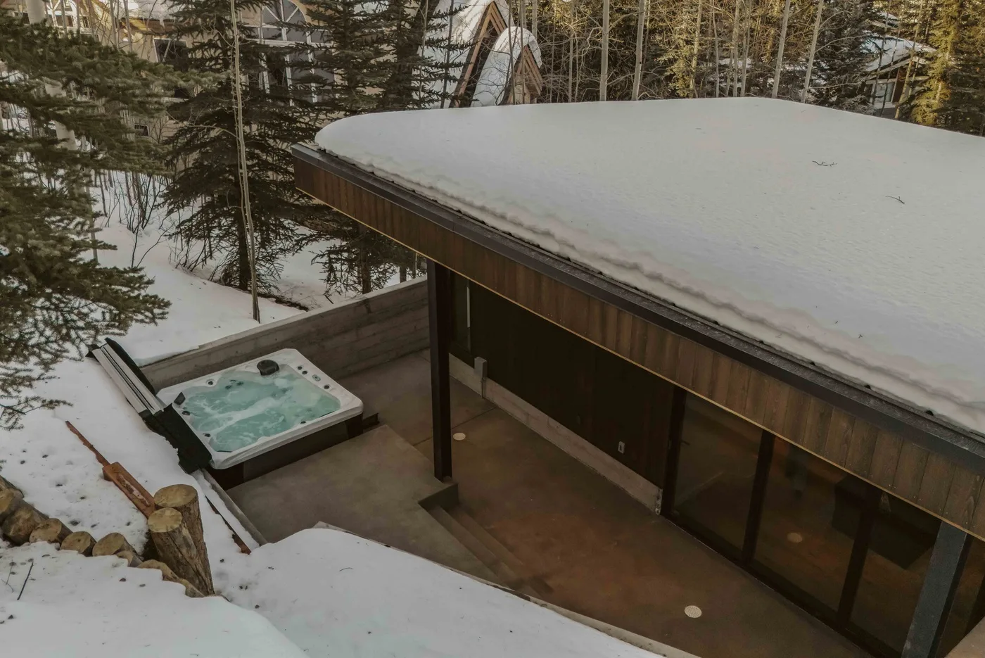 Un patio exterior cubierto de nieve con una bañera de hidromasaje junto a un edificio moderno.