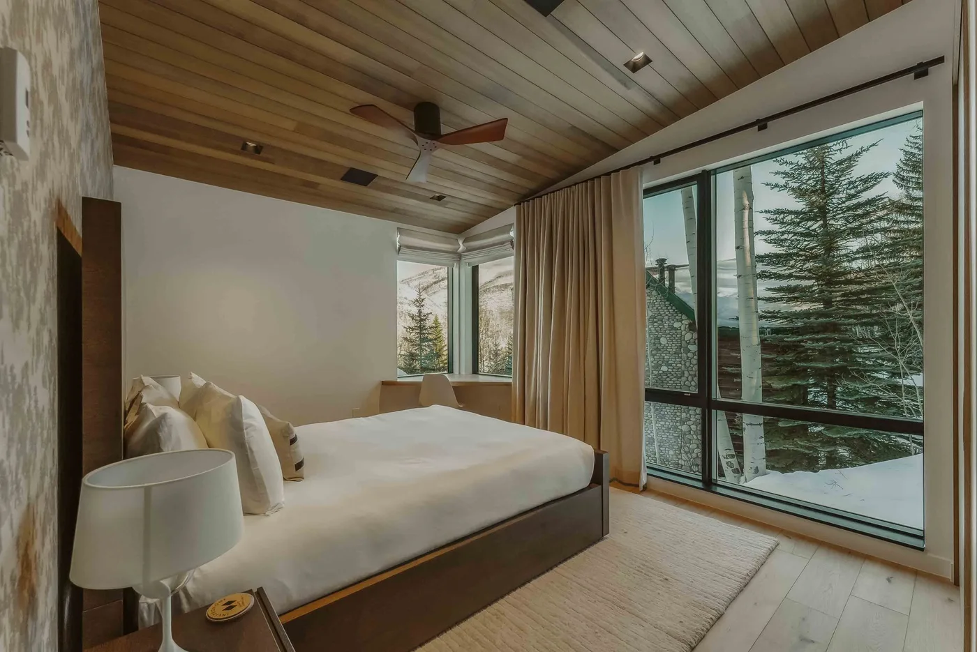 Un dormitorio con una cama junto a grandes ventanas con vistas a los árboles.
