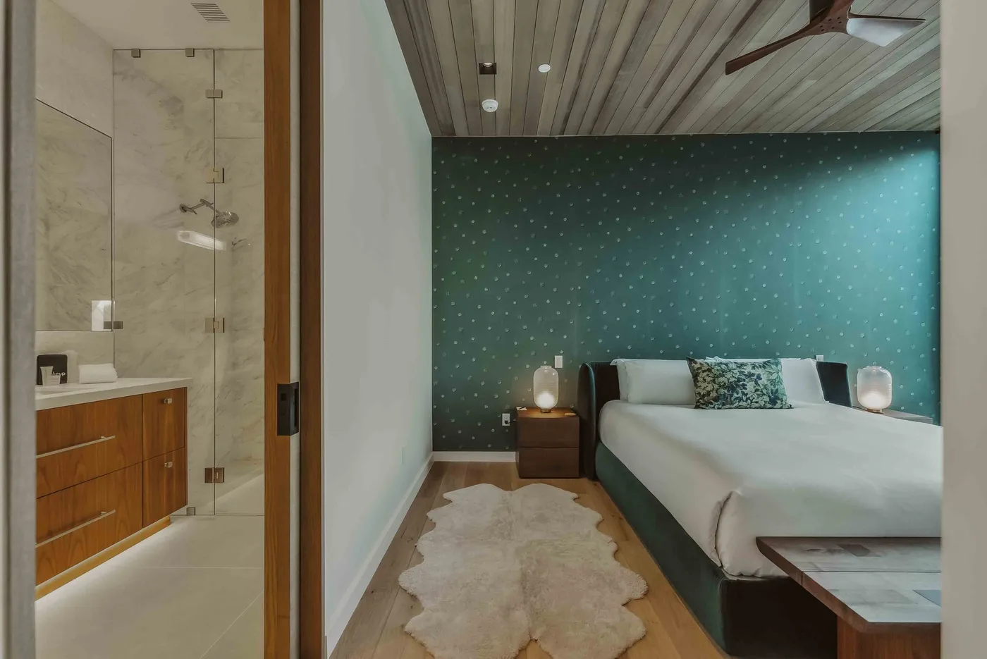 Un dormitorio con una pared decorativa verde azulado y un baño contiguo.