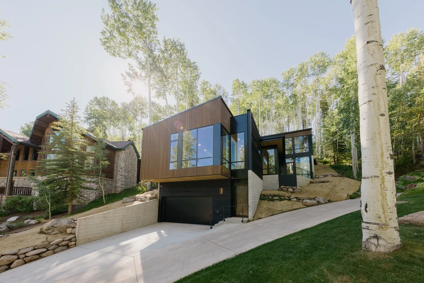 Una casa moderna con grandes ventanas está entre árboles junto a una entrada inclinada.