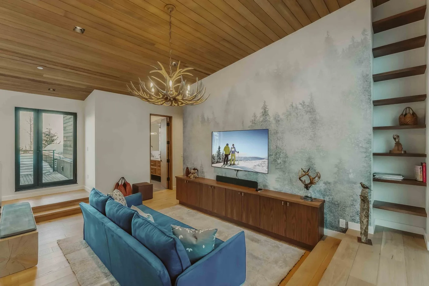 Una sala de estar con asientos azules, un televisor en la pared y un techo de madera.