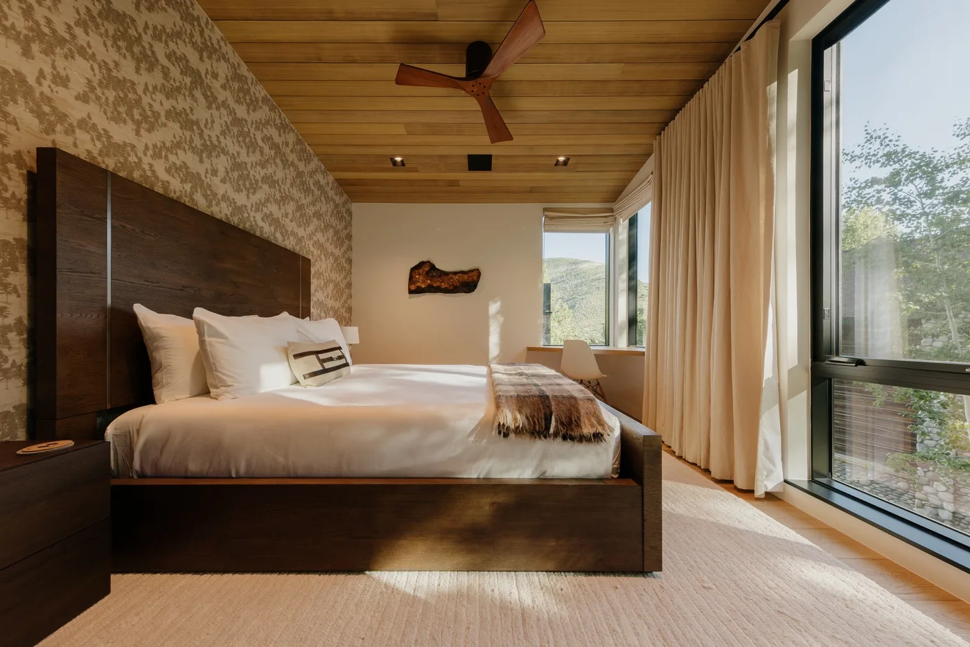 Un dormitorio con una cama grande y ventanas con vistas a la vegetación.