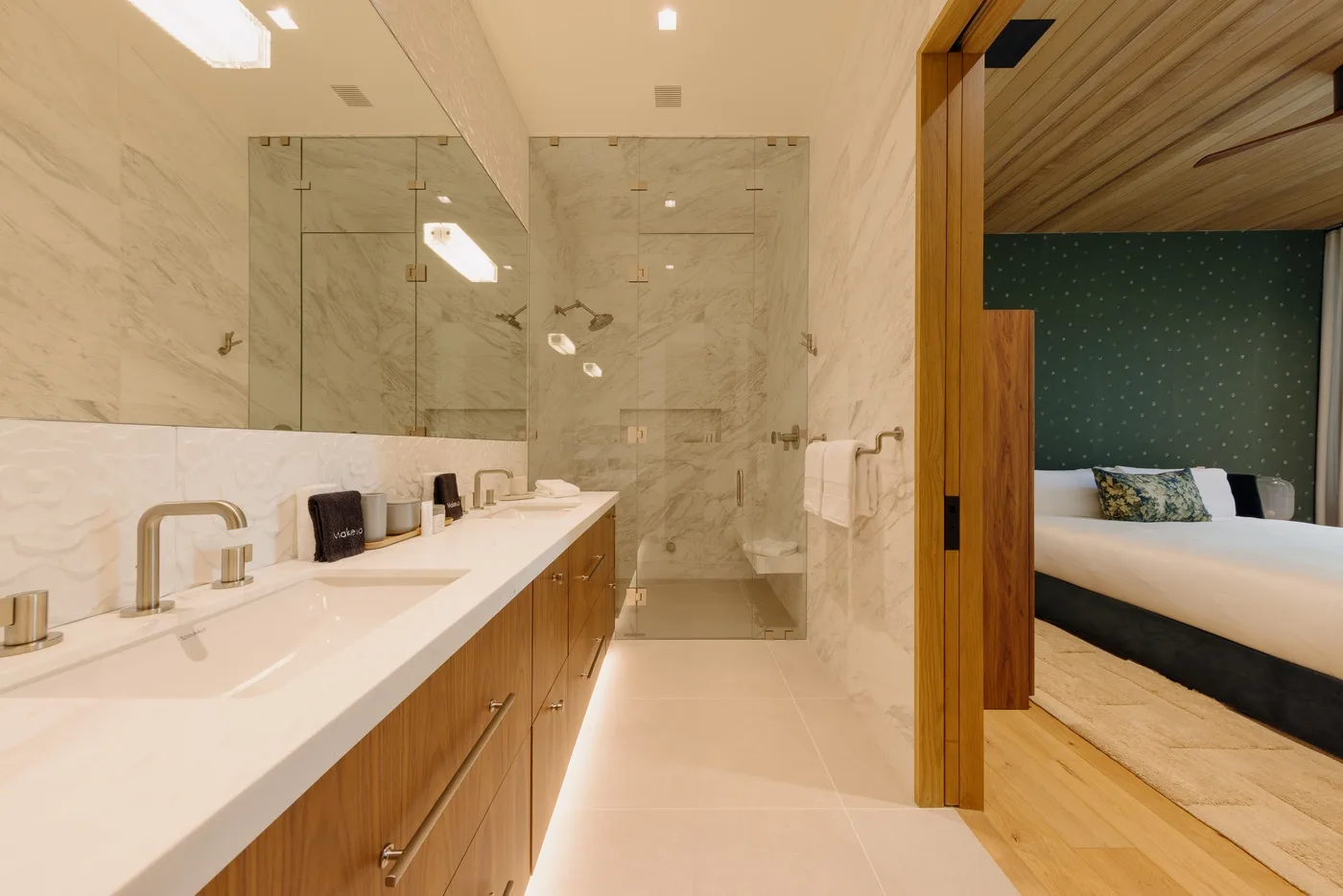 Un baño luminoso con un tocador largo y una ducha de vidrio junto a un dormitorio.