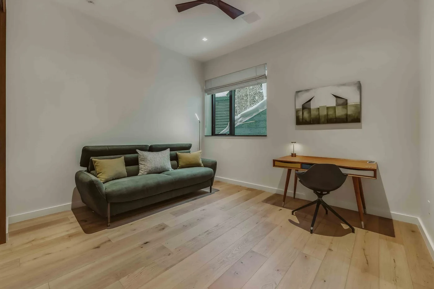 Una sala luminosa con un sofá y un escritorio pequeño junto a la ventana.