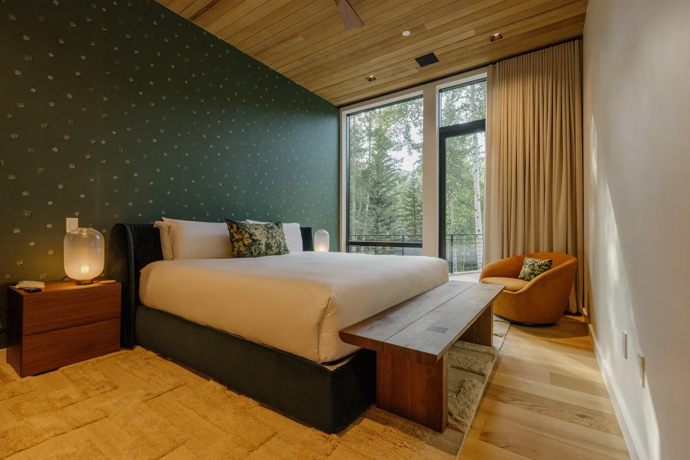 Un dormitorio con una cama grande junto a ventanales y una pequeña zona de estar.