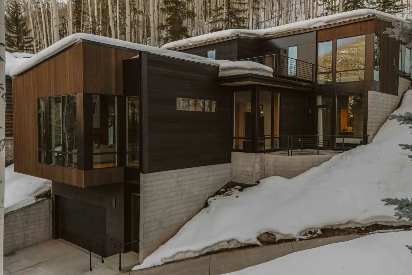 Una casa moderna con grandes ventanas está entre árboles cubiertos de nieve.