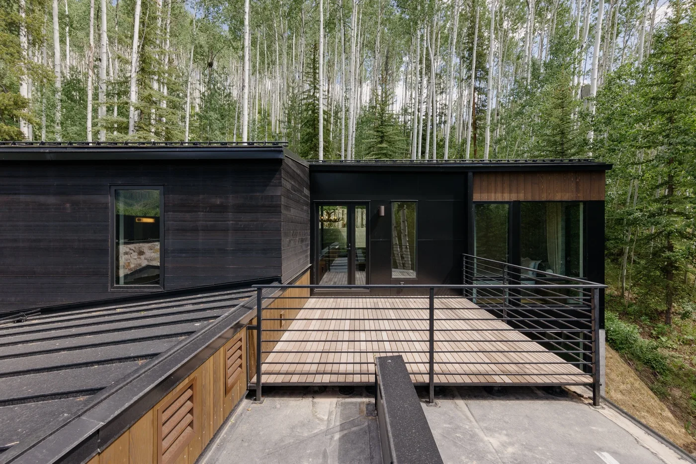 Una casa moderna oscura da a una terraza de madera rodeada de árboles.