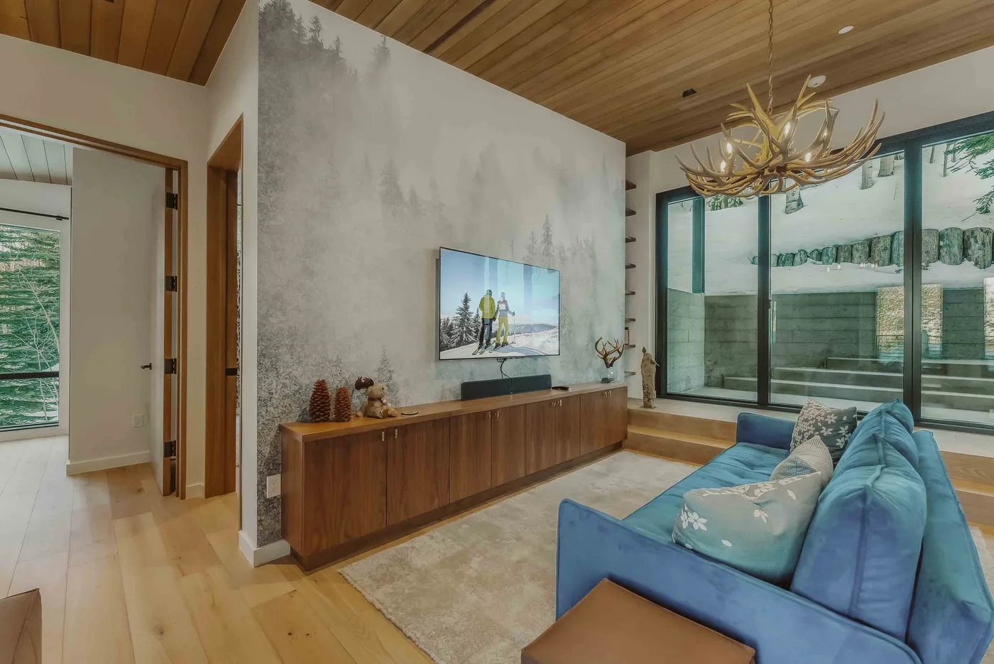 Una sala de estar con asientos azules, un televisor y grandes ventanales.