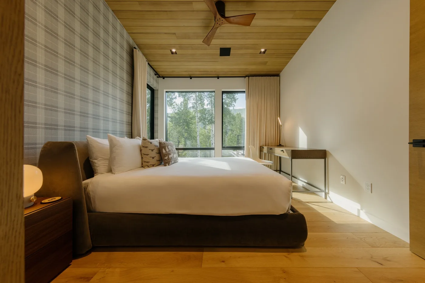 Un dormitorio con una cama grande frente a ventanas con vistas a los árboles.