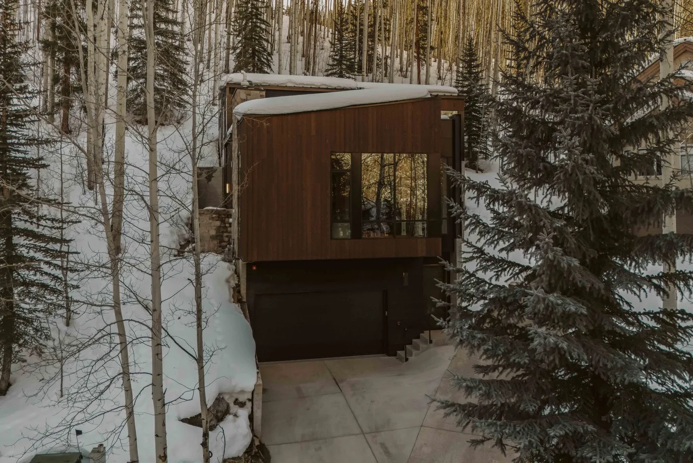 La entrada de un edificio revestido de madera está entre árboles cubiertos de nieve.