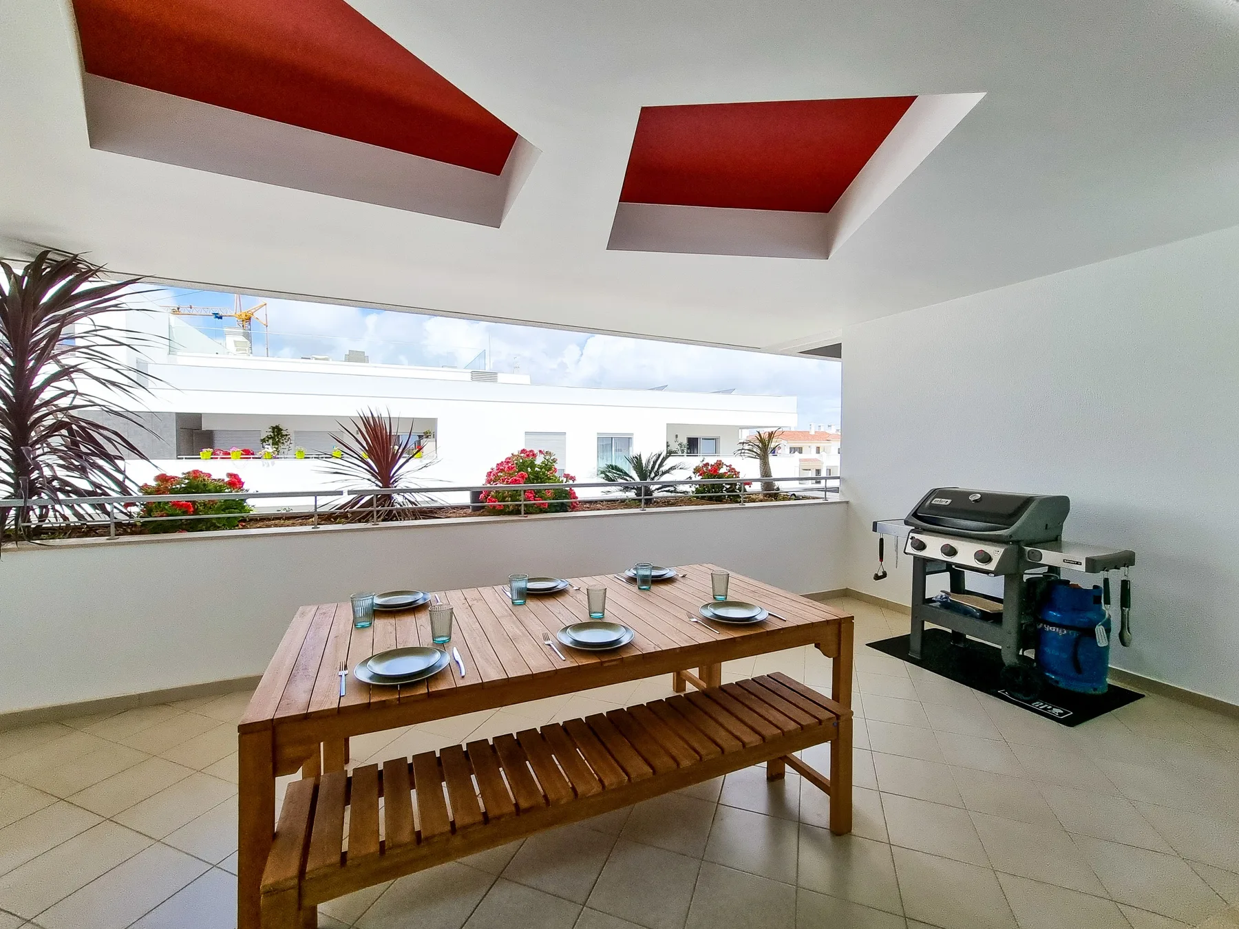 Una terraza cubierta tiene una mesa de comedor de madera y una parrilla.
